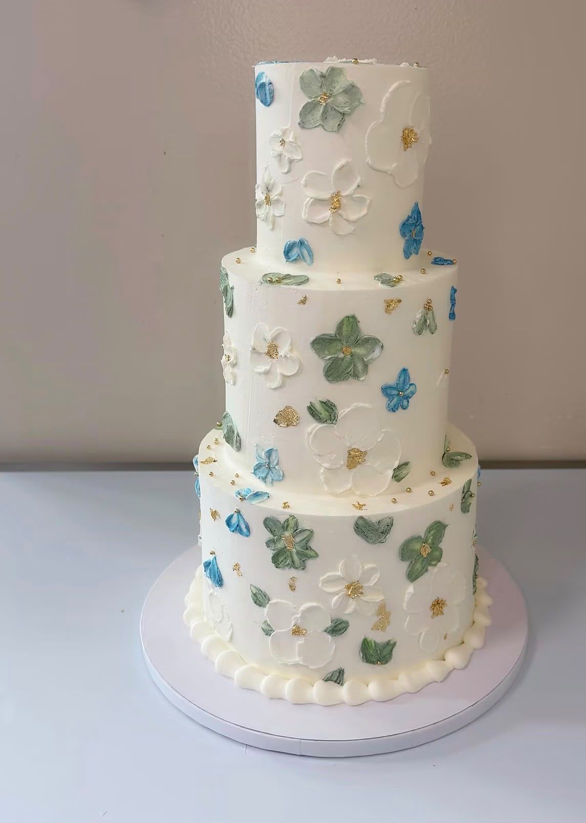Tarta de boda de tres pisos con flores pintadas a mano en crema y detalles de pan de oro