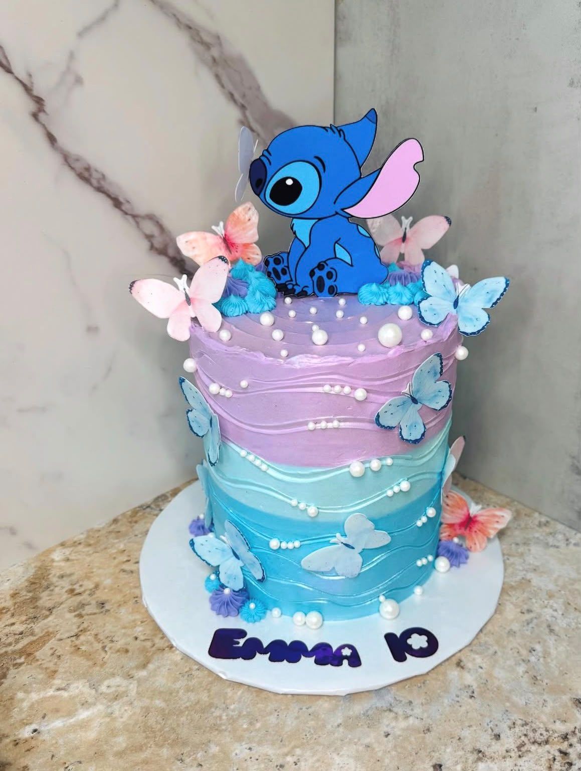 Tarta de cumpleaños en degradado lila y azul con mariposas, perlas y topper de Stitch