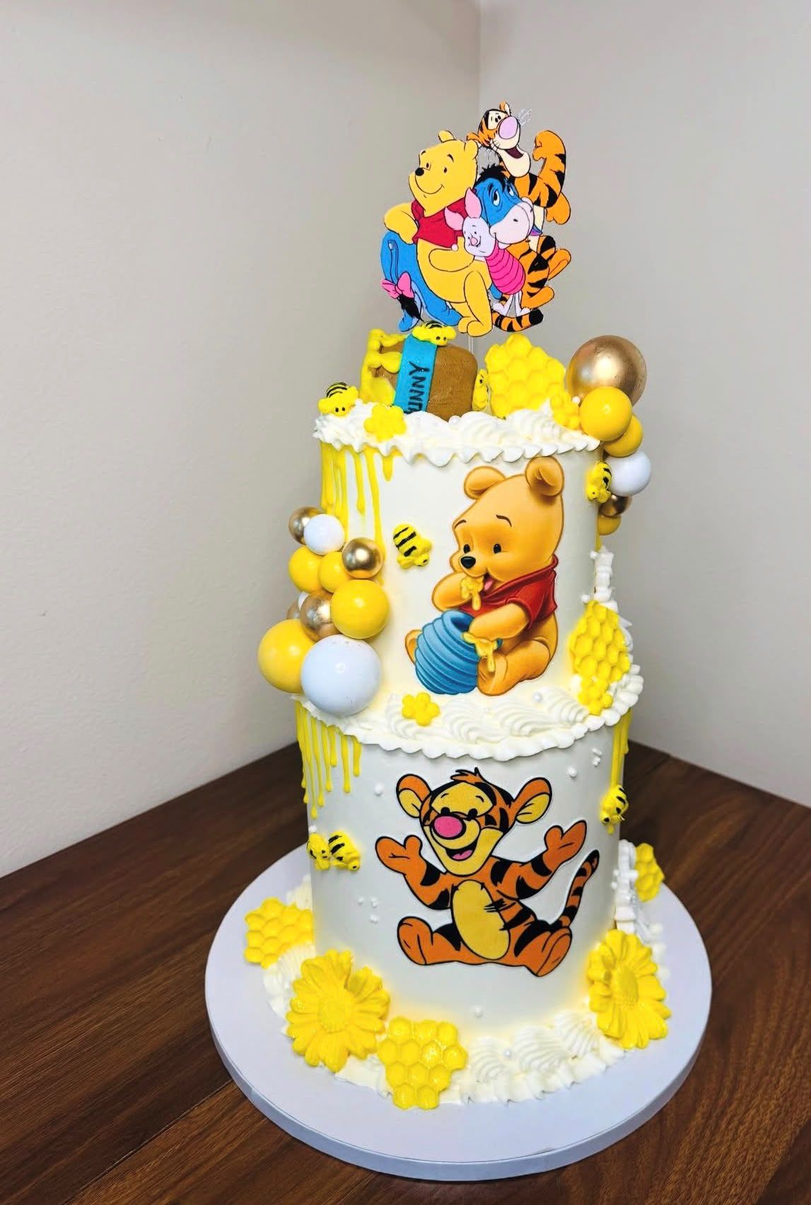 Tarta de dos pisos de Winnie the Pooh con drip amarillo, panales y esferas doradas